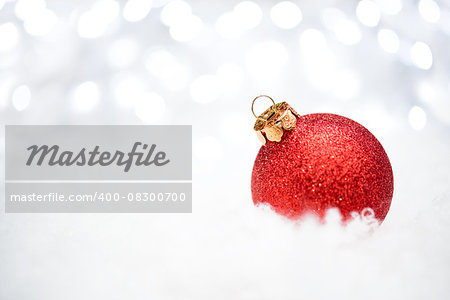 Christmas Decoration with Red Ball in the Snow on the Blurred Background with Holiday Lights. Greeting Card with Space for Your Text