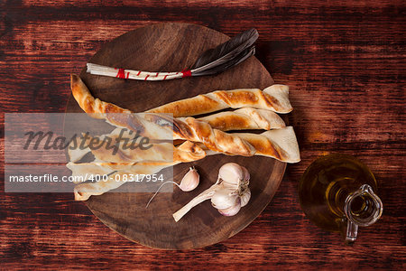 Pizza breadsticks with garlic and olive oil on wooden chopping board on brown wooden background, top view. Gastronomy background.