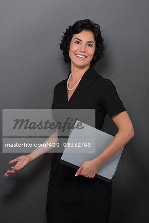 Portrait of attractive young businesswoman in black holding files. Smiling lady telling something interesting isolated on grey.