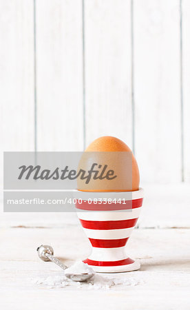 Brown egg in stripy egg cup on white wooden background.