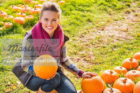 Portrait of smiling beautiful woman holding pumpkins on the pumpkin patch on farm during the autumn season