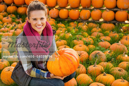 Portrait of smiling woman sitting and holding big pumpkin on farm during the autumn season