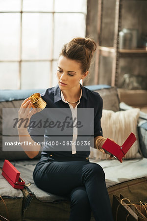 Wealthy elegant brunette woman unpacking and checking new jewelry while sitting on sofa in modern loft apartment. Luxurious life concept