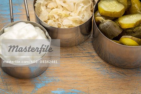 sauerkraut, cucumber pickles and yogurt - popular probiotic fermented food - three measuring cups against rustic wood