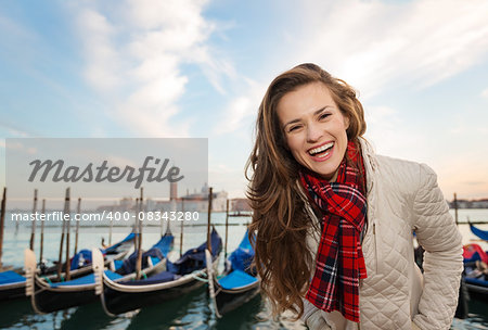 Sunset brings to life irresistible magic of Venice - the unique Italian city. Portrait of happy young woman traveler standing on embankment in the front of the line of gondolas