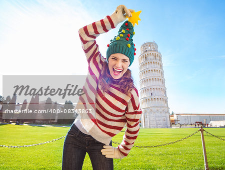 Young, itching from energy and searching for excitement. I'm going to Christmas trip to Italy. It is a no-brainer. Smiling woman make fun of Christmas tree hat in front of Leaning Tour of Pisa