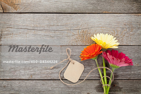 Three colorful gerbera flowers with tag on wooden table