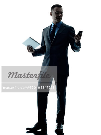 one caucasian business man standing using digital tablet and telephone silhouette isolated on white background