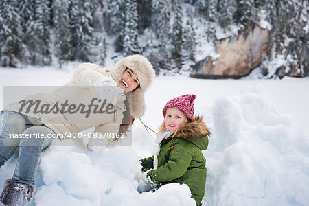 Winter outdoors can be fairytale-maker for children or even adults. Happy mother pointing in camera to child while playing outdoors