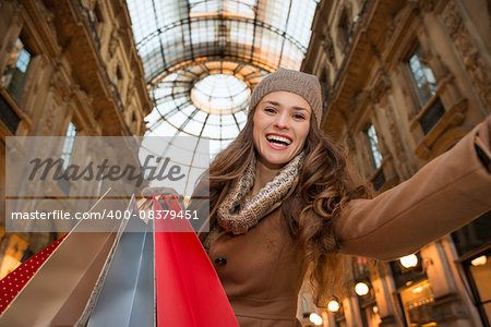 Get ready to making your way through shopping addicted crowd. Huge winter sales in Milan just started. Smiling young woman with shopping bags taking selfie in Galleria Vittorio Emanuele II