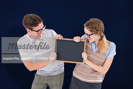 Geeky hipster couple holding little blackboard against navy blue