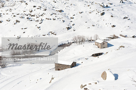 Remote stone mountain hut on an alpine slope next to river covered in snow