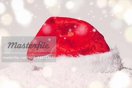 red decorative christmas santa hat on snow against grey festive background