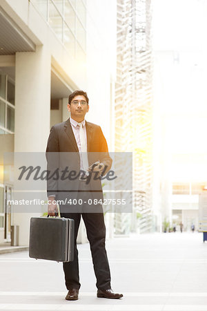 Portrait of fullbody Asian Indian business man standing outside modern office building block, beautiful golden sunlight at background.