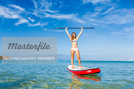 A beautiful and happy woman with arms up and learning paddle-surf