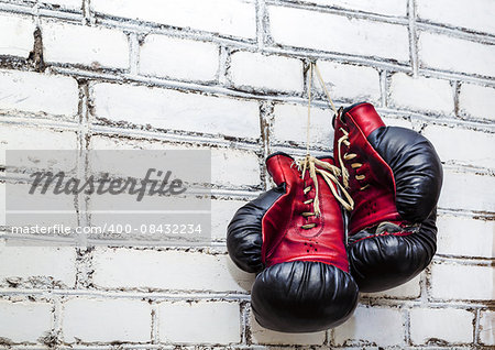 A pair of old boxing gloves hanging on white brick wall background.