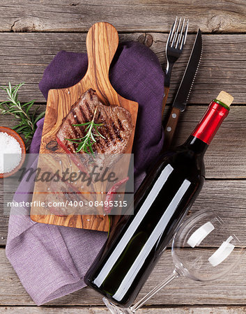Grilled beef steak with rosemary, salt and pepper and wine bottle on wooden table. Top view