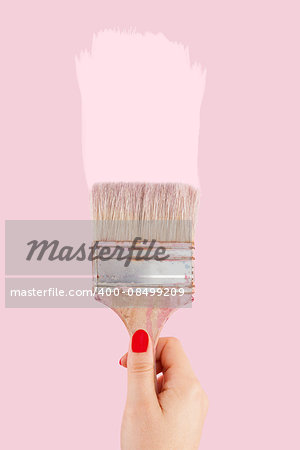 Female hand with red fingernails holding paintbrush isolated on pink background. Creative painting.