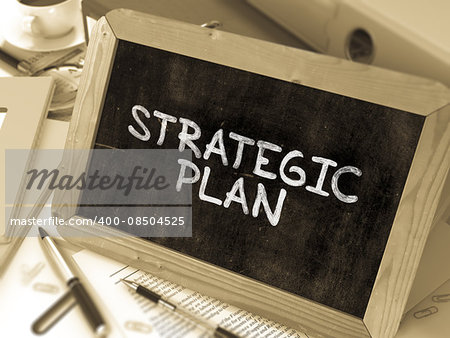 Strategic Plan Handwritten by white Chalk on a Blackboard. Composition with Small Chalkboard on Background of Working Table with Office Folders, Stationery, Reports. Blurred, Toned Image. 3D Render.