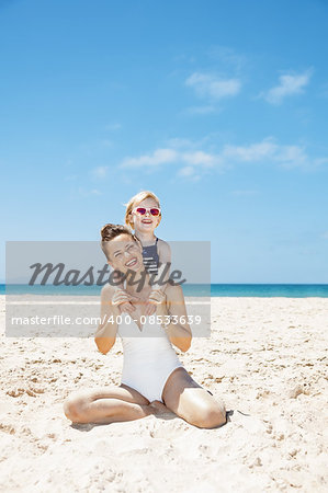 Family fun on white sand. Portrait of happy mother and girl in swimsuits at sandy beach on a sunny day