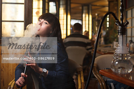 Concept: leisure lifestyle. Beautiful young woman with hookah in a bar restaurant
