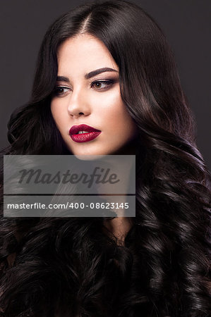 Beautiful brunette model with curls, classic makeup and red lips. The beauty of the face. Portrait shot in the studio on a gray background.