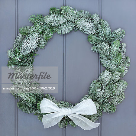 Snow covered christmas wreath of blue spruce fir with white bow on grey wood front door background.