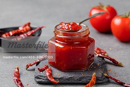 Tomato and chili sauce, jam, confiture in a glass jar on a grey stone background.