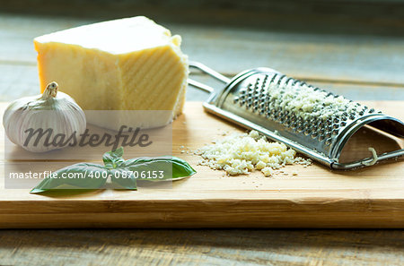 Heap of grated Parmesan on wooden background with leaf of basilic, garlic and  with grater.Close up shot