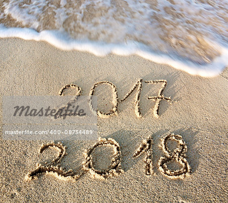 2017 2018 inscription written in the wet beach sand with sea water wave. Inscription 2017 and 2018 on a beach sand, the wave is almost covering the digits 2017.