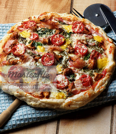 Delicious Mushrooms Pizza with Forest Chanterelles, Bacon, Tomatoes, Basil and Cheese on Blue Napkin with Pizza Cutter closeup on Wooden background