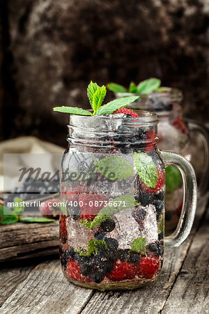 Detox drink with fresh berries, mint and ice in glass jars on wooden background