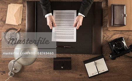 Vintage businessman in the office reading a contract sitting at his desk, top view