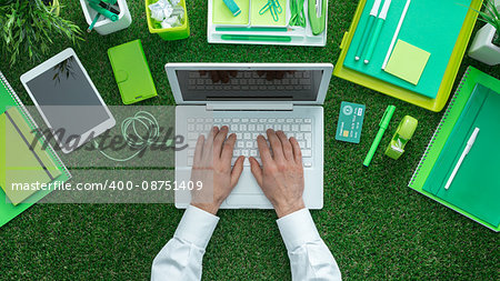 Businessman using a laptop and networking on the grass; green business, sustainability and communication concept