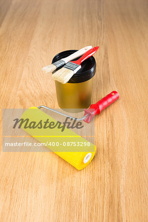 Paint roller, brushes and color bucket on hardwood floor ready for painting.