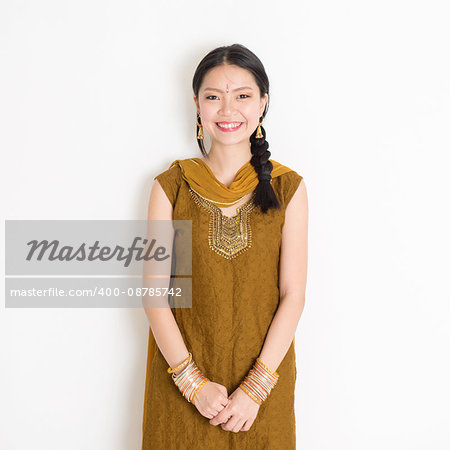 Portrait of young mixed race Indian Chinese woman in traditional Punjabi dress smiling, standing on plain white background.