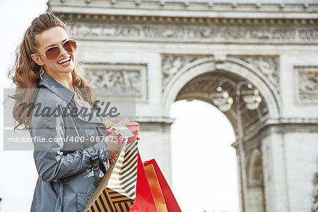Stylish Christmas in Paris. Portrait of happy young woman in sunglasses with shopping bags and Christmas present near Arc de Triomphe in Paris, France