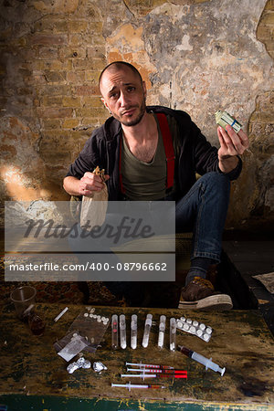 Drug dealer holding profit from selling drugs. Drug dealer looking at camera while many drugs lying on table in front of him.
