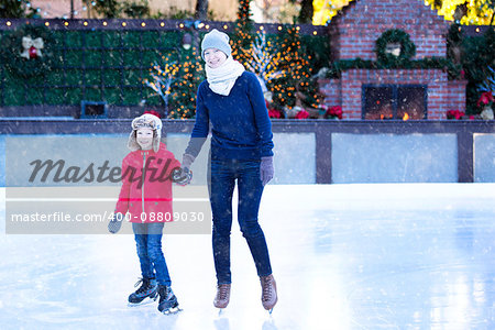 family of two enjoying ice skating at winter at outdoor skating rink decorated for holiday time at snowy weather, winter and family concept