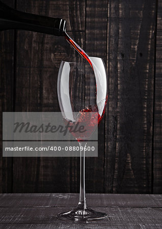 Pouring red wine into the glass from bottle on old wooden background