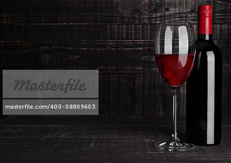 Bottle and glass of red wine with reflection on wooden background