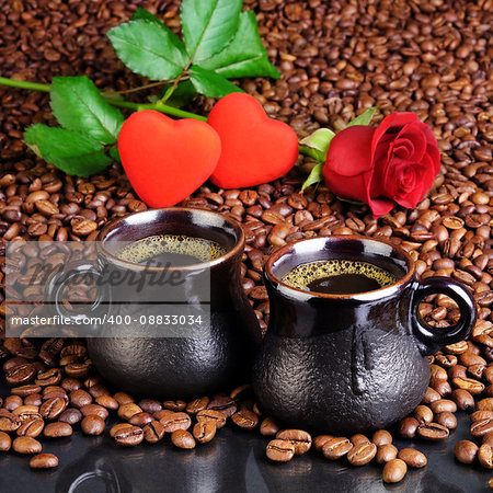 Two cups of black coffee with foam on the background from the fried coffee beans, small hearts and a red rose. For cards for Valentine's Day.