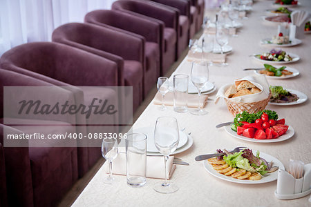 a table covered with a white tablecloth with salads, glasses, plates, napkins and a number of seats