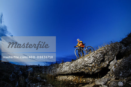 Mountain biker in action across rocks against blue sky concept for healthy lifestyle, exercise and extreme sports