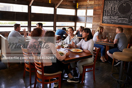 Four female friends at lunch in busy restaurant, full length