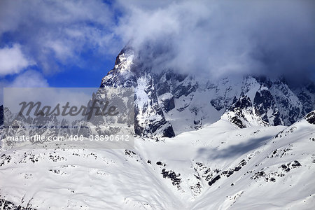 Mount Ushba in fog at sun winter day before storm. Caucasus Mountains. Svaneti region of Georgia.