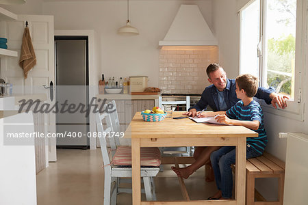 Father Helping Son With Homework Sitting At Kitchen Table