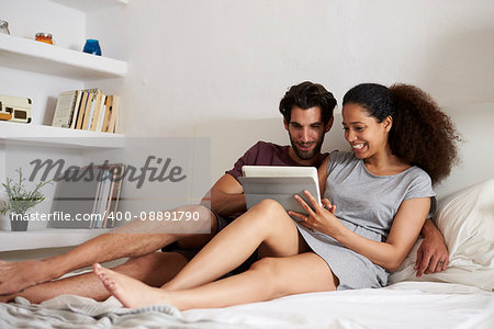 Couple Sitting On Bed Looking At Digital Tablet Together