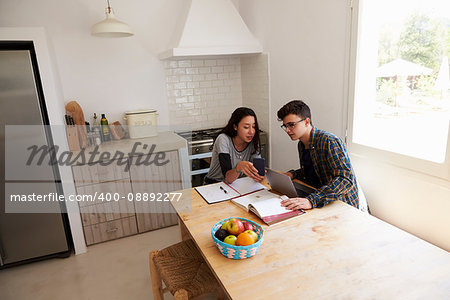Teenagers study with laptop and phone in kitchen, elevated view