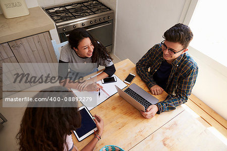 Three teens study in kitchen using computers, elevated view